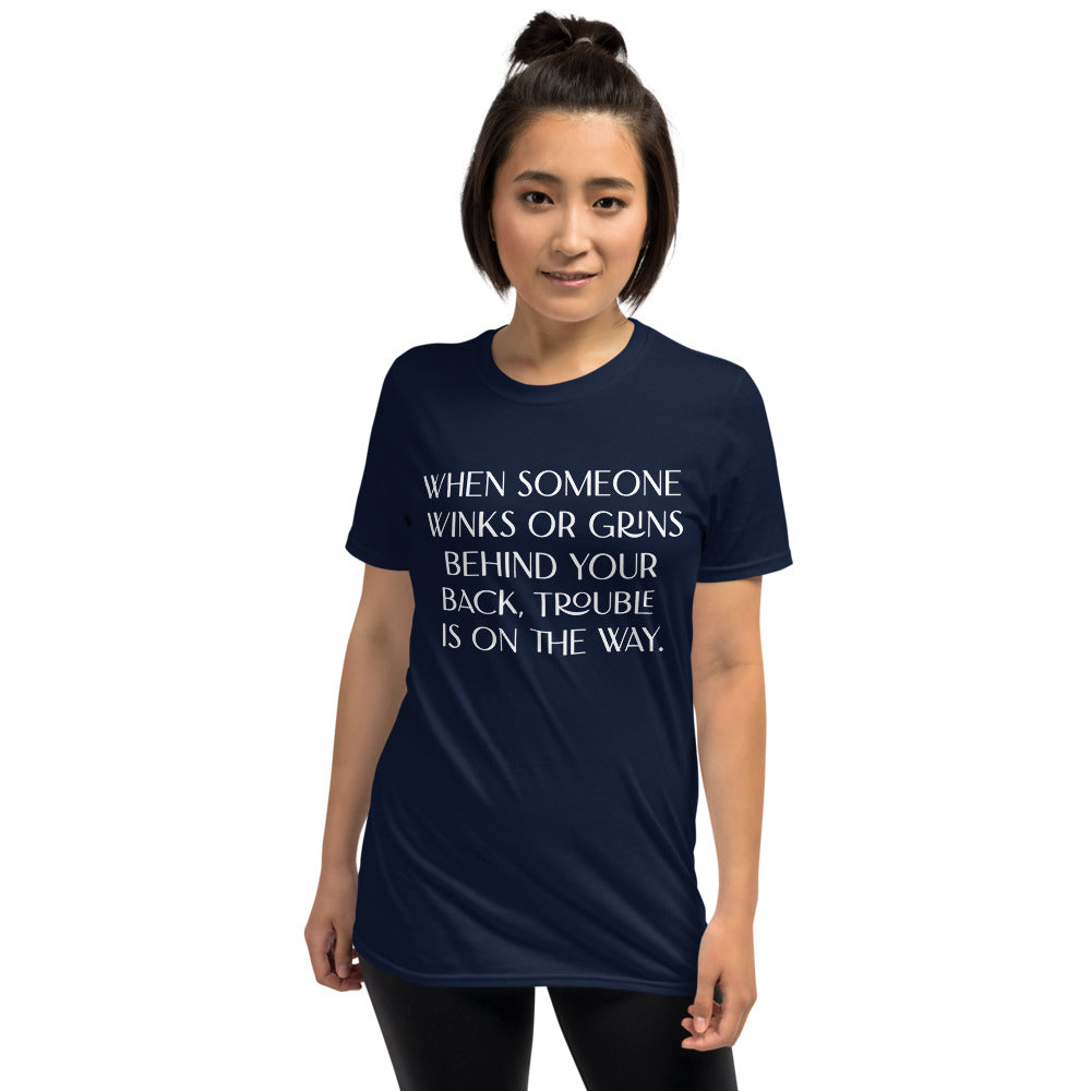 Unisex soft-style Navy T-shirt with WHEN SOMEONE WINKS OR GRINS BEHIND YOUR BACK, TROUBLE IS ON THE WAY in White letters