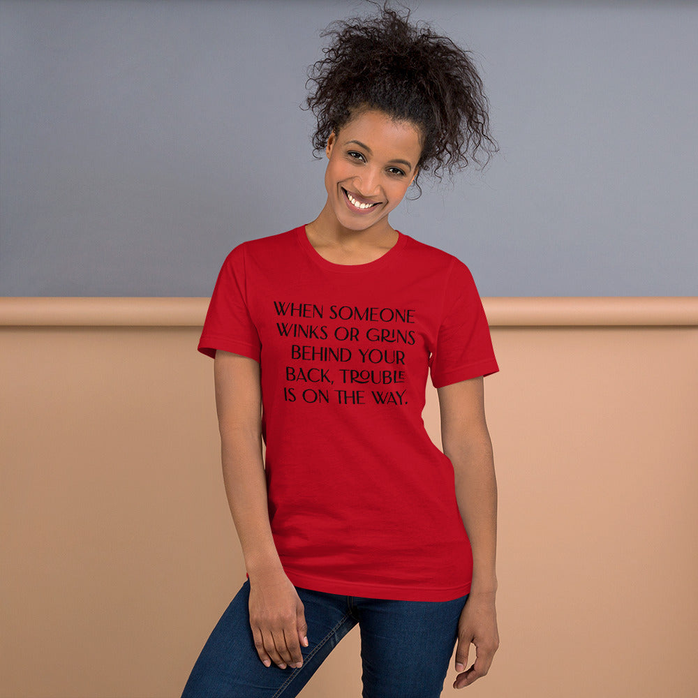Unisex Red T-Shirt has When Someone Winks or Grins Behind Your Back, Trouble is On the Way in Black letters