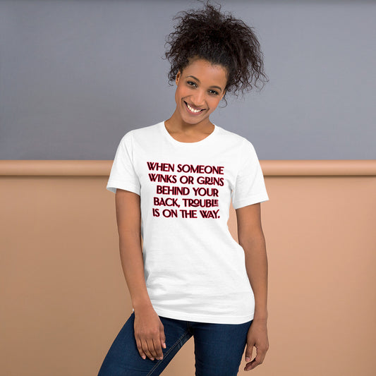 Unisex White T-shirt has When Someone Winks or Grins behind Your Back, Trouble is on The Way in Red letters